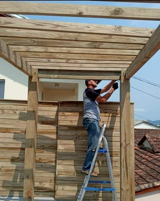 Carpinteiro construindo estrutura de madeira para pergolado em ambiente externo.