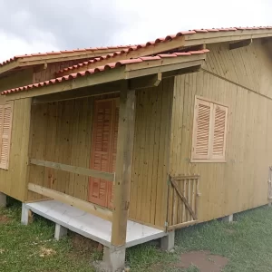 Cabanas de madeira com telhado colonial, janelas venezianas e varanda frontal em acabamento rústico.
